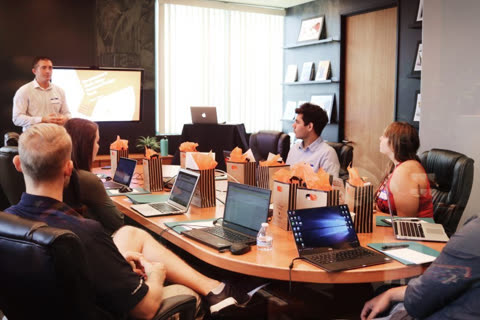 Man presenting to a group seated around a conference table.