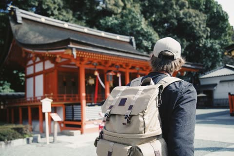 Person with backpack facing away from a red building.