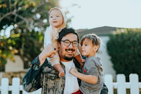Man carrying two children on his shoulders outdoors.
