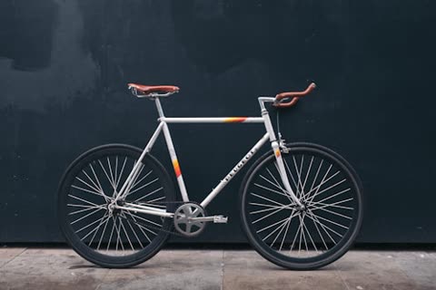 White bicycle with brown seat and handlebars rests against a dark wall.